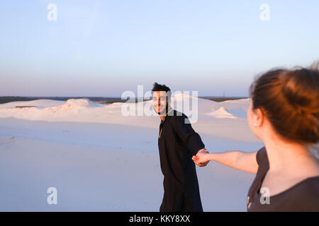 Die stattlichen männlichen arabischen Holding Frau Hand, plaudern und lächelte ihr suchen. Liebhaber durch weite sandige Wüste bei Sonnenuntergang unter offenen blauen Spaziergang s Stockfoto