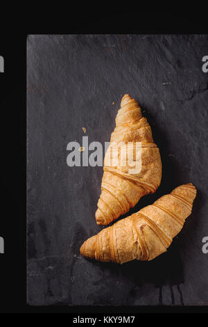 Zwei frisch gebackene Croissants auf schwarzem Schiefer. Ansicht von oben. Stockfoto