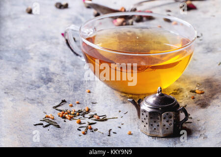 Vintage Tee Sieb als Teekanne und Glas Tasse heißen Tee mit trockenen grüne Teeblätter. alte Zinn backgtound. Stockfoto