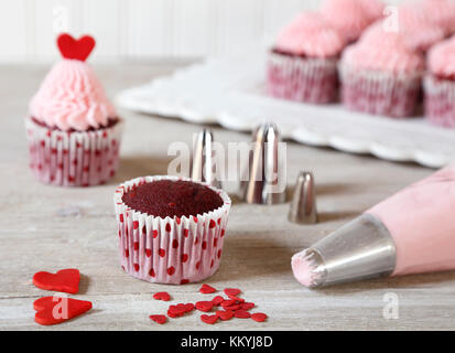 Dekorieren red velvet Cupcakes mit rosa Zuckerguss und roten Herzen zum Valentinstag. Stockfoto