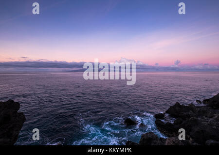 Meer zusammenhaengen Felsen an der Westküste von Teneriffa, La Gomera am Horizont, unter einem violetten Himmel bei Dämmerung, Kanarische Inseln, Spanien Stockfoto