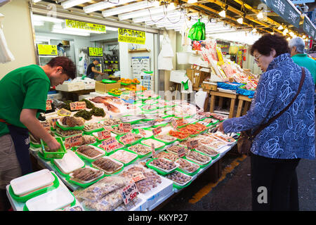 Tsukiji, Tokio, Japan - 17. Januar 2023 : ein japanischer Fischhändler bereitet frische Meeresfrüchte zum Verkauf zu und der Kunde kauft Fisch am Fischstand Stockfoto