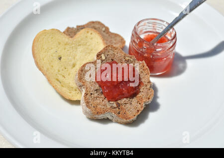 Stücke von inländischen, selbstgebackenes Brot mit Vollkorn und ein kleines Glas mit köstlichen wild strawberry jam Stockfoto