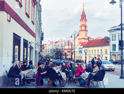 Vilnius, Litauen - 1. April 2017: Touristen in open air Street Cafe in der Altstadt in Vilnius, Litauen. Kirche St. Nikolaus auf der b Stockfoto