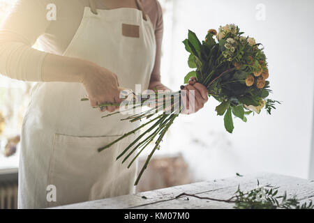 Junge weibliche florist Trimmen eines gemischten Blumenstrauß während an einem Tisch in Ihrem Blumenladen arbeiten Stockfoto