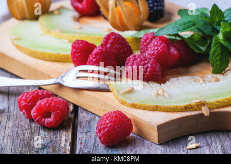 Mischung aus Himbeeren, Brombeeren, Minze, Physalis und Melone auf Holz Schneidebrett über Holz- Tabelle. Stockfoto