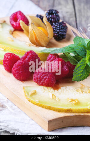 Mischung aus Himbeeren, Brombeeren, Minze, Physalis und Melone auf Holz Schneidebrett über Holz- Tabelle. Stockfoto