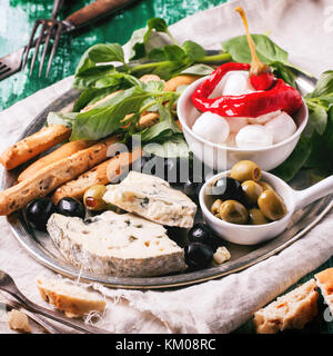 Gemischte antipasti Blau Käse, Oliven und Mozzarella serviert auf silbernem Tablett über grüne Holztisch mit Vintage Gabeln. square Bild mit selektiven Fokus Stockfoto