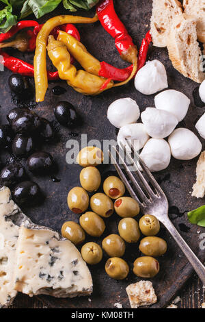 Gemischte Antipasti eingelegte Paprika, Oliven und Mozzarella serviert auf gusseisernen Brett über Holztisch mit Vintage Gabel. top View Stockfoto