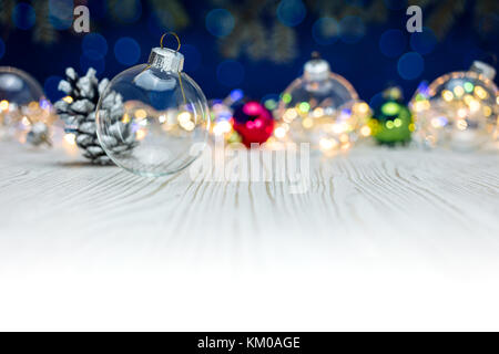 Christbaumkugeln auf weißem rustikalen Tisch gegen unscharfe bunte Lichter Hintergrund Stockfoto