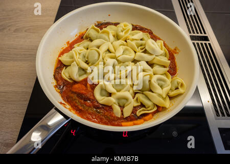 Pfanne mit Tortellini und Tomatensauce auf einem Kochfeld Stockfoto