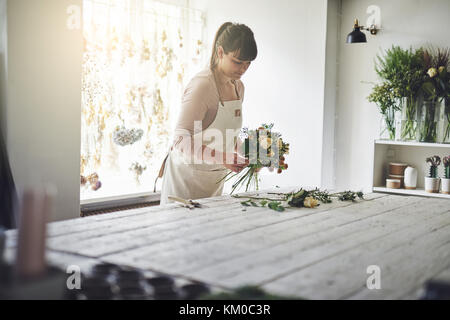 Junge weibliche Blumenhändler an einem Tisch arbeitet sie in ihrem Blumenladen einen Blumenstrauß aus gemischten Blumen Stockfoto