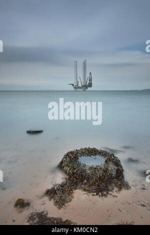 Lange Belichtung Bild des abndoned Reifen am Ufer mit einer Jack-up Oil Rig in der Ferne. Stockfoto