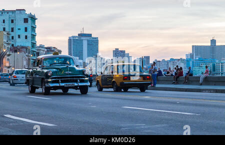 Taxis der kontrastierenden Generationen einander in der Dämmerung auf dem Malecon Ocean Highway in Havanna im November 2015. Das grüne Auto von verursacht wird Stockfoto