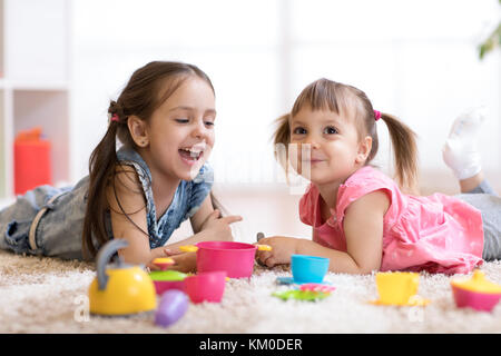 Süße kleine Kinder spielen mit Küchenutensilien, während auf dem Boden liegend zu Hause Stockfoto