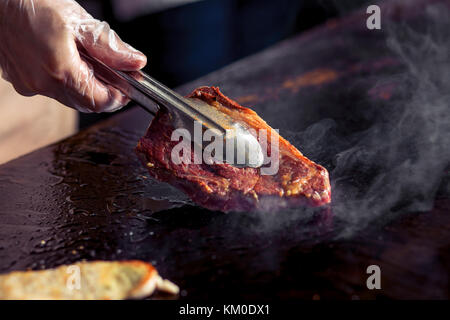 Zangen halten gebratenes Fleisch. Koch bereitet Schweinefleisch Stockfoto