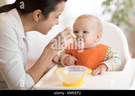 Essen, Kind und Elternschaft Konzept - Mama mit Püree und Löffel füttern Babys zu Hause Stockfoto