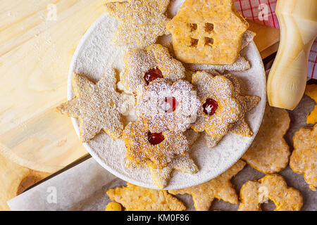 Hausgemachte Lebkuchen und Shortbread Cookies in verschiedenen Formen sterne haus Blume mit Marmelade Linzer in Pulverform auf Platte Backblech Holz Nudelholz gemütliche Festi Stockfoto