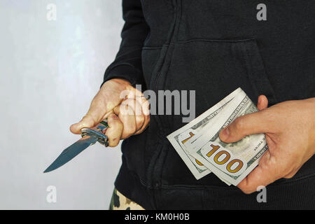 Ein Verbrecher mit einem Messer in der Hand und Dollar. ihr Taschengeld zu schützen. Die Drohung eines Messers. Nacht Einbruch. Erpressung von Geld. 100 Stockfoto