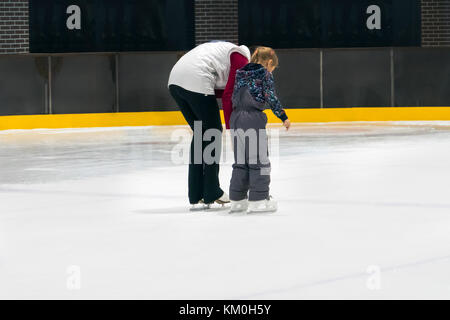 Happy Family indoor Eislaufen am Eislaufplatz. Winter Aktivitäten. Junge Mädchen Ausbilder unterrichtet, ein kleines Mädchen zu Skate. Mutter und Tochter halten sich an den Händen Stockfoto