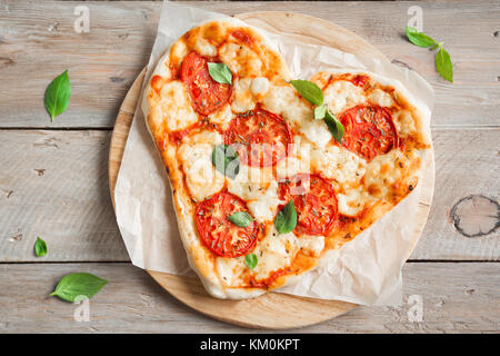 Herzförmigen Pizza Margherita über Holz- Hintergrund mit Kopie Raum. Pizza mit Tomaten, Mozzarella und Basilikum zum Valentinstag. Stockfoto