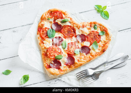 Pizza in Herzform über Holz- Hintergrund mit Kopie Raum. Pizza mit Tomaten, Peperoni, Mozzarella und Basilikum zum Valentinstag. Stockfoto