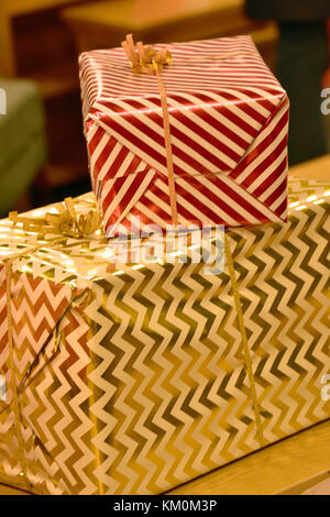 Große Weihnachtsgeschenke oder Geschenke in glänzendem Metall gestreiften roten und goldenen Geschenkpapier mit Schleife in goldenen Faden mit Bogen gebunden. festliche Themen. Stockfoto