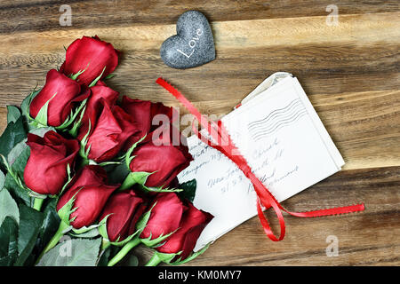 Langstielige rote Rosen mit einem Stapel alte Briefe mit roter Schleife und Karte ein wenig Stein Herz mit dem Wort Liebe gebunden. Stockfoto