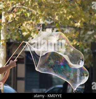 Eine riesige, schillernde Blase mit Seife, Wasser und Luft, die von zwei Menschen mit Bambus gemacht. Nur ihre Arme sind dargestellt. Stockfoto