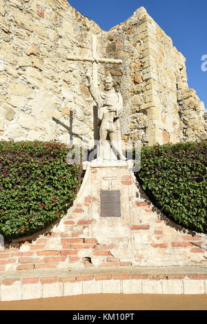 San Juan Capistrano, CA - 1. Dezember 2017: Vater Junipero Serra mit indischer Kinderstatue, auf dem Missionsgelände mit den Ruinen der Great Stone Church. Stockfoto