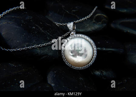 Weißes Gold Anhänger mit Perlmutt und Diamanten auf schwarzen Steinen Hintergrund Stockfoto