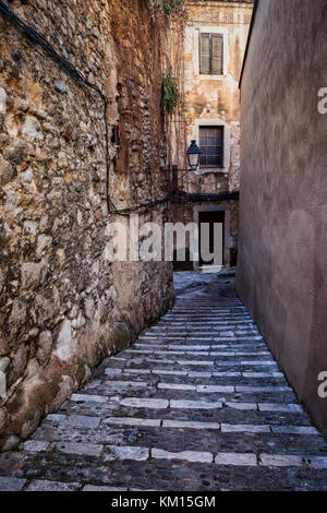 Enge gepflasterte Gasse mit Treppen entlang der mittelalterlichen Mauer aus Stein im alten jüdischen Viertel - der Ruf in Girona, Katalonien, Spanien Stockfoto