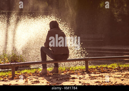 Frau sitzt auf Zaun und Suchen am Brunnen Stockfoto