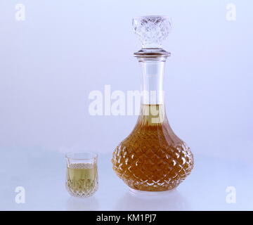 Crystal decanter und ein kleines Glas mit einer goldenen Flüssigkeit auf einem weißen Hintergrund Bild im Querformat mit Kopie Raum gefüllt Stockfoto
