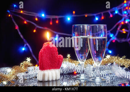 Neues Jahr Karte mit Weihnachten dekorative Kerze santa claus Handschuh und 2 Sektgläser über Girlande bokeh hellen Hintergrund Stockfoto