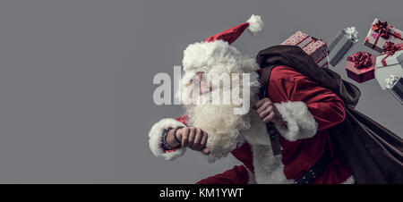 Lustiger Weihnachtsmann laufen und die Weihnachtsgeschenke, er ist Prüfung Zeit und verlieren Geschenke aus seinem Sack. Stockfoto