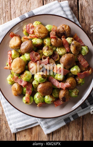 Hausgemachten Salat von gebratenen Kastanien, Rosenkohl und Speck closeup auf einem Teller. Senkrechte Draufsicht von oben Stockfoto