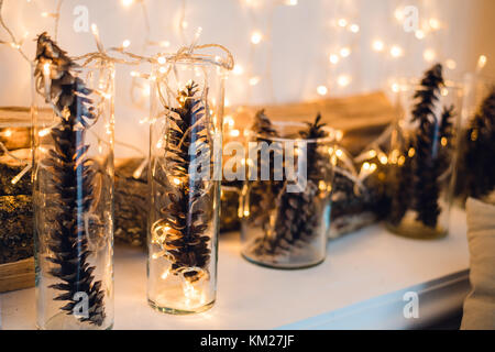 Weihnachten oder Neujahr Zusammensetzung mit Girlanden in kleinen Glas Leuchter und Tannenzapfen, Holz- Bars auf einem Hintergrund, festlichen Abend, selektiver Fokus Stockfoto