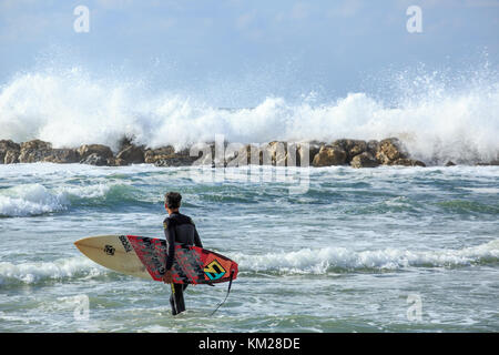 Die jungen Surfer in das Meer mit einem Surfbrett an einem windigen Tag in Tel Aviv, Israel Stockfoto