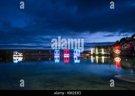 Blick auf die Lichter des Mousehole-Hafens - weihnachtsbeleuchtung - vor der offiziellen Einschaltung, wobei die Lichter nachts im Wasser reflektiert werden. Stockfoto