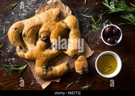 Eine köstliche Focaccia-brot mit schwarzen Oliven und Rosmarin auf einem rustikalen Tischplatte. Stockfoto