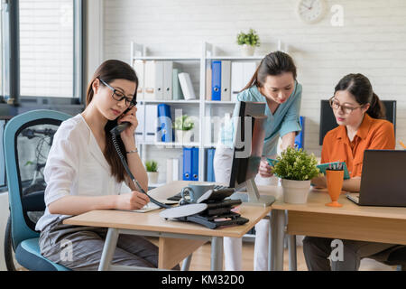 Schöne junge Manager, am Telefon zu sprechen für ein neues Projekt während zwei Kollegen im Hintergrund zu diskutieren. Stockfoto