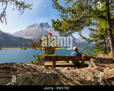 Mann sitzt auf einer Bank, liest ein Buch vor einem Berg See Stockfoto