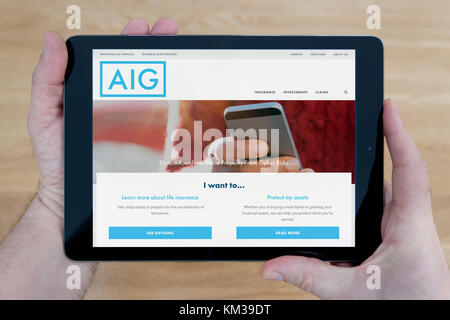 Ein Mann schaut auf die AIG Website auf seinem iPad tablet device, Schuß gegen einen hölzernen Tisch top Hintergrund (nur redaktionelle Nutzung) Stockfoto