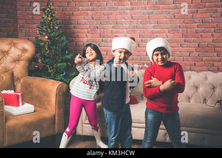 Indische Kinder feiern Weihnachten - süße kleine indische Kinder spielen, lachen und Spaß mit Geschenksets zu Weihnachten, sitzen auf dem Boden oder Sofa wi Stockfoto