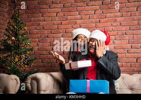 Happy indischen reifer Mann und Mädchen mit Weihnachtsbaum zu Hause und saß auf dem Sofa und den Austausch von Geschenkbox. Happy indische Familie zu Hause während Weihnachten Stockfoto