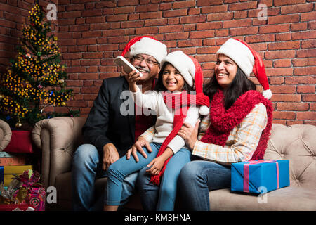 Familie, Urlaub, Generation, Weihnachten und Personen Konzept - lächelnd indischen Großeltern und Enkelin mit geschenkboxen Sitzen auf der Couch zu Hause Stockfoto