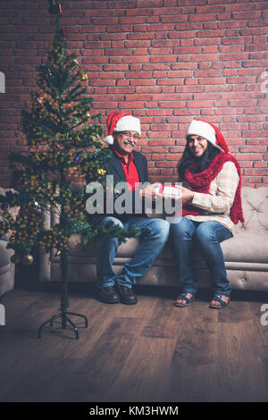 Im mittleren Alter indischer smart Paar feiern Weihnachten und den Austausch von Geschenken beim Sitzen auf dem Sofa Stockfoto