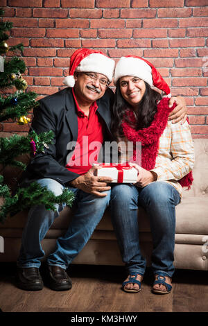 Im mittleren Alter indischer smart Paar feiern Weihnachten und den Austausch von Geschenken beim Sitzen auf dem Sofa Stockfoto