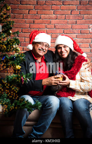 Im mittleren Alter indischer smart Paar feiern Weihnachten und den Austausch von Geschenken beim Sitzen auf dem Sofa Stockfoto
